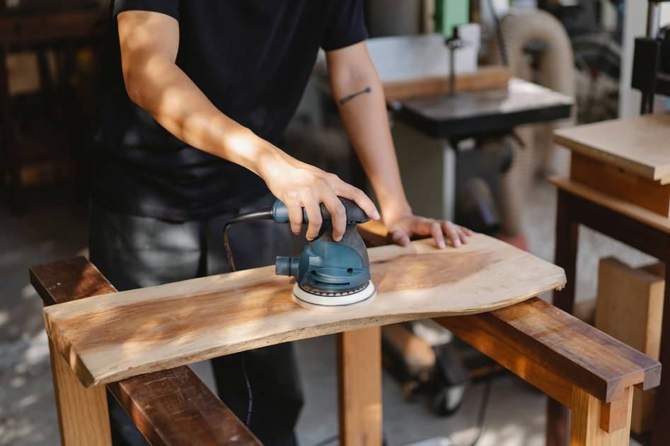 Random orbit sander smoothing wooden surface with dust extraction